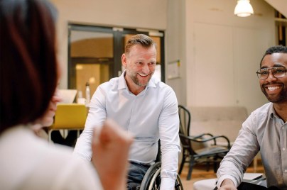 Disabled worker in wheelchair smiling with co-workers